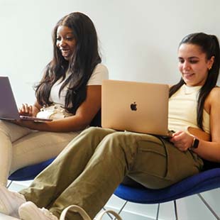 two students laughing and working on laptops
