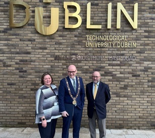 An image of three people standing in front of a bronze TU Dublin logo