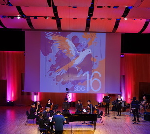 An orchestra performing in front of a graphic with the dove of peace and SDG 16 SDG