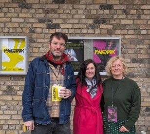 A group of people pose in front a brick wall with posters that have text saying Paradox