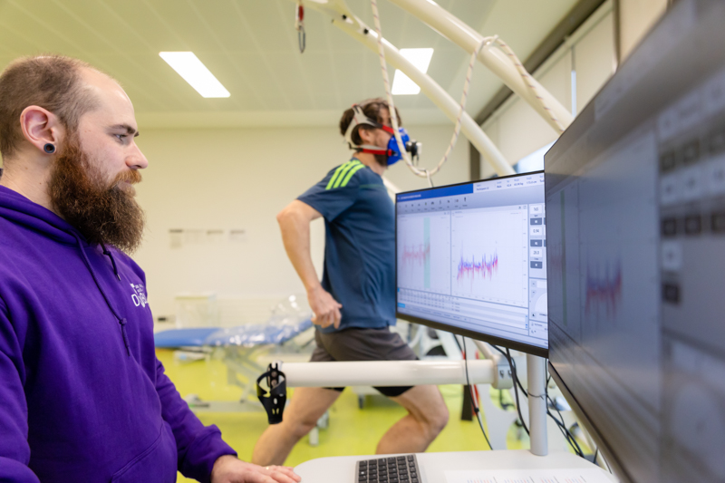 Two researchers in a TU Dublin lab conducting an experiment, one observing and one running on a treadmill while data displays on two monitors