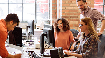 Three smiling employees looking at a computer screen