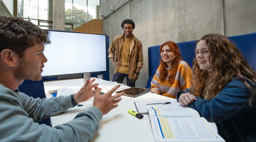 four students sitting around table with screen